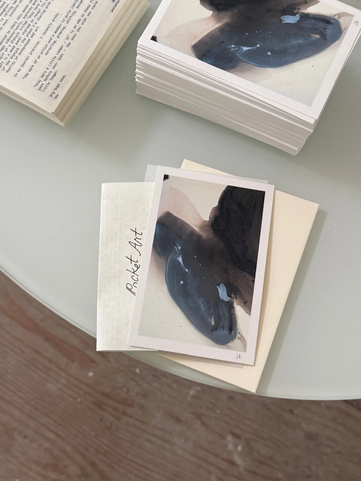 Stacks of Pocket Art prints with dark blue and brown abstract shapes beside printed notes.